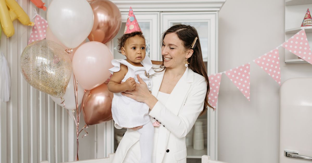 Adulte portant un bébé en tenue blanche lors d'une fête décorée de ballons