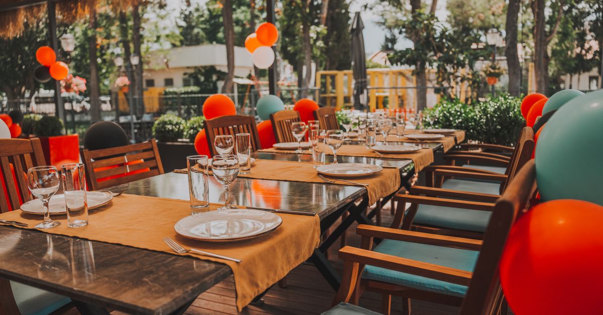 Grande table de fête dressée en extérieur avec ballons et assiettes, prête pour une réception de baptême