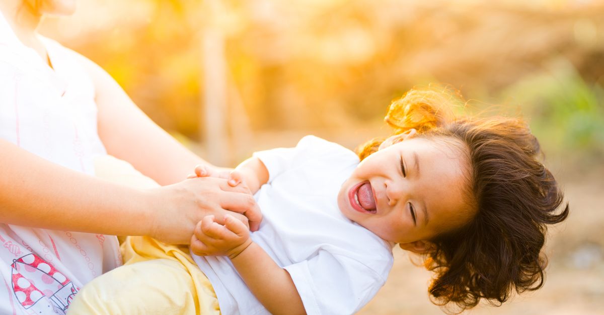 Jeune femme faisant rire un jeune enfant dans ses bras en plein air, complicité de marraine