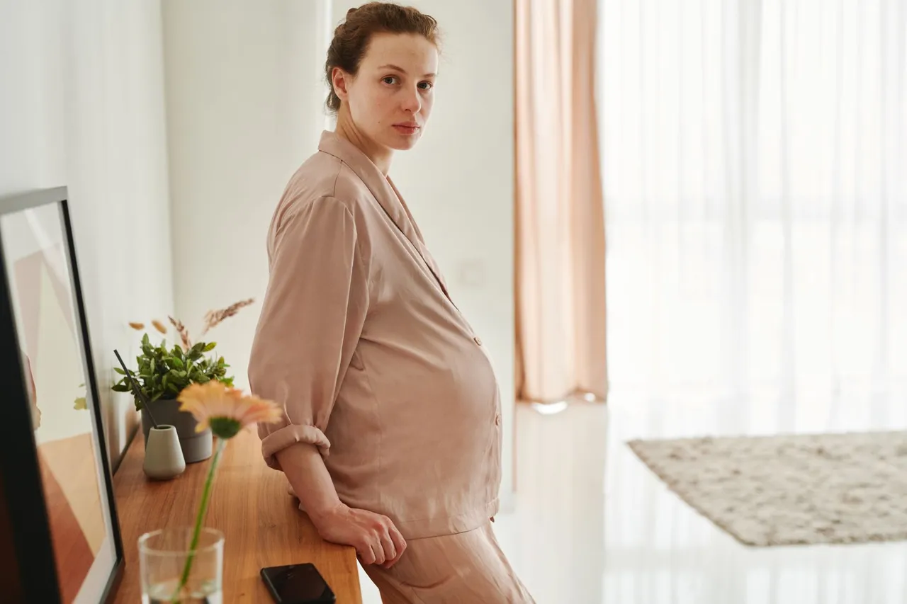 Une femme enceinte debout dans une chambre lumineuse en fin de grossesse