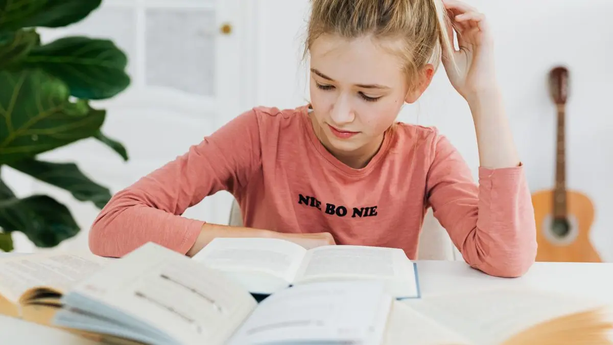 Une adolescente concentrée révise avec ses livres ouverts sur son bureau