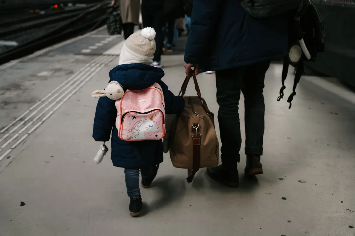 Enfant avec son sac à dos et son doudou marchant avec son parent sur un quai de gare