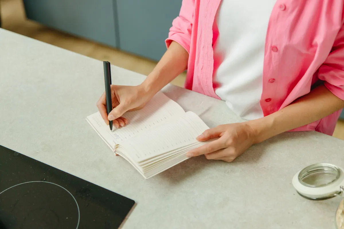 Femme notant ses démarches dans un carnet sur le plan de travail de la cuisine