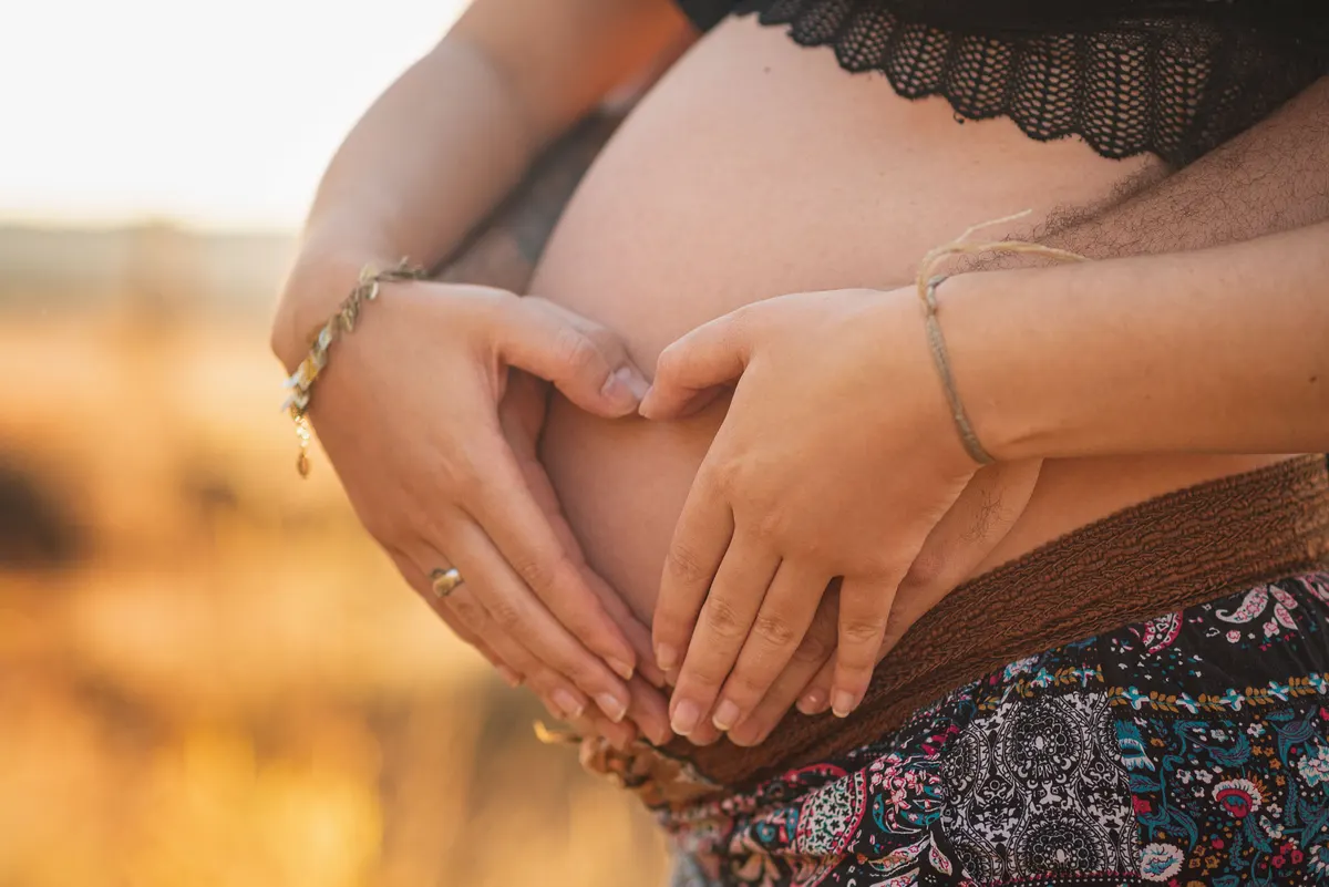 Mains formant un cœur sur le ventre d'une femme enceinte au soleil couchant