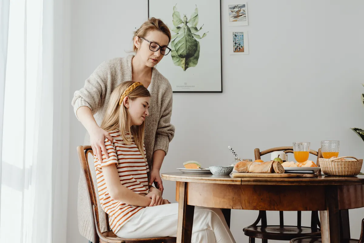 Mère réconfortant sa fille adolescente à la table du petit-déjeuner