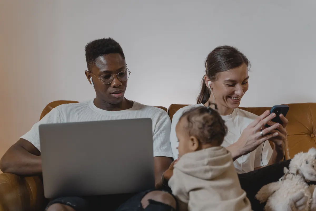 Parents sur le canapé avec leur bébé, ordinateur portable et téléphone en main
