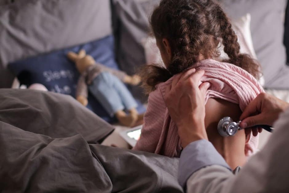 Médecin auscultant le dos d'une jeune enfant avec un stéthoscope, à domicile
