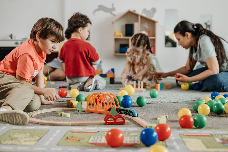 Groupe d'enfants qui jouent ensemble au sol avec une éducatrice dans une salle de crèche
