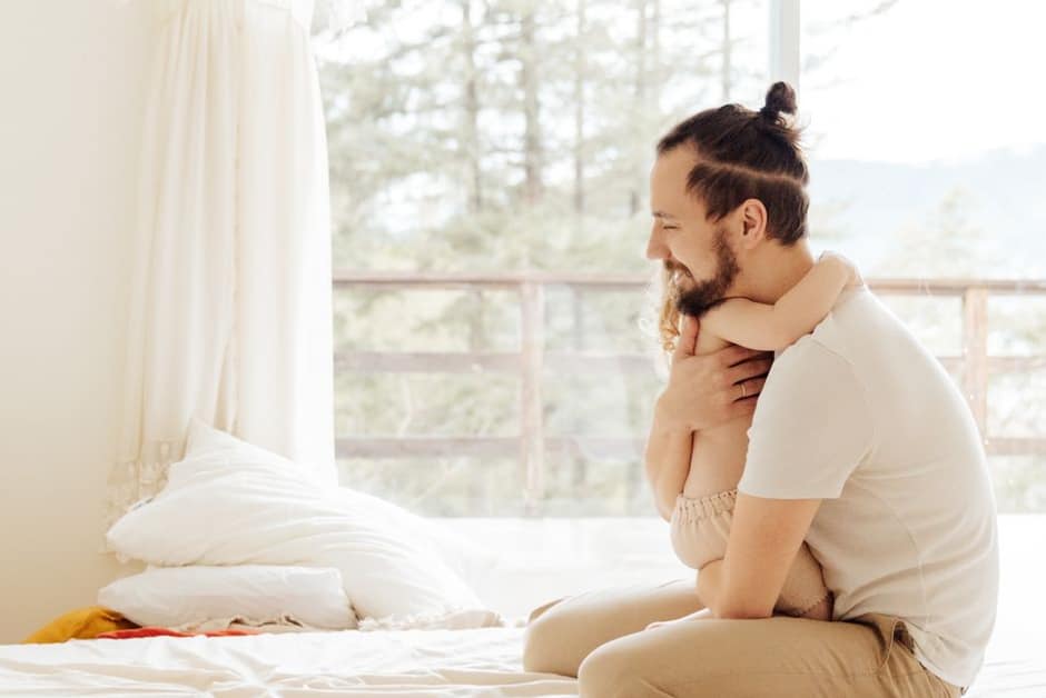 Parent tenant son jeune enfant endormi et calme dans ses bras, dans un salon