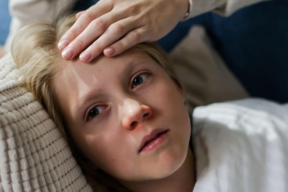 Parent posant la main sur le front d'un enfant allongé sur le canapé, au moment de décider école ou maison