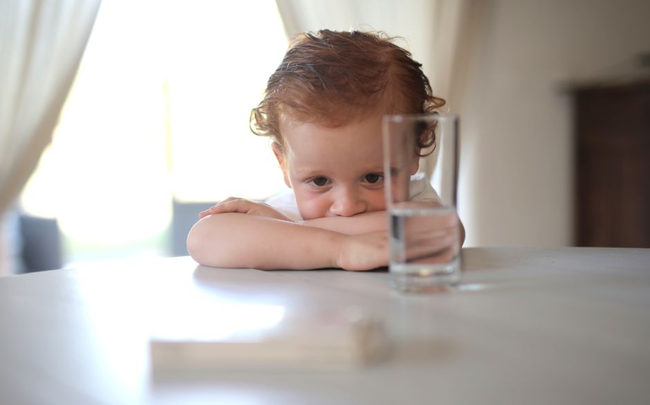 Jeune enfant accoudé à une table, regardant un verre d'eau, illustrant l'hydratation pendant une gastro-entérite