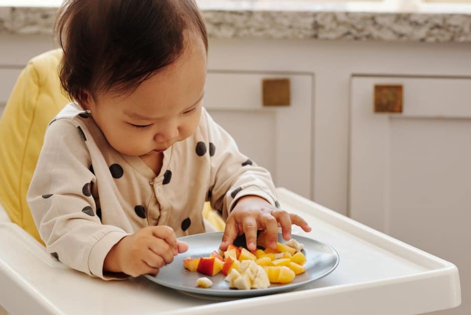 Tout-petit mangeant des morceaux de fruits et de banane dans sa chaise haute