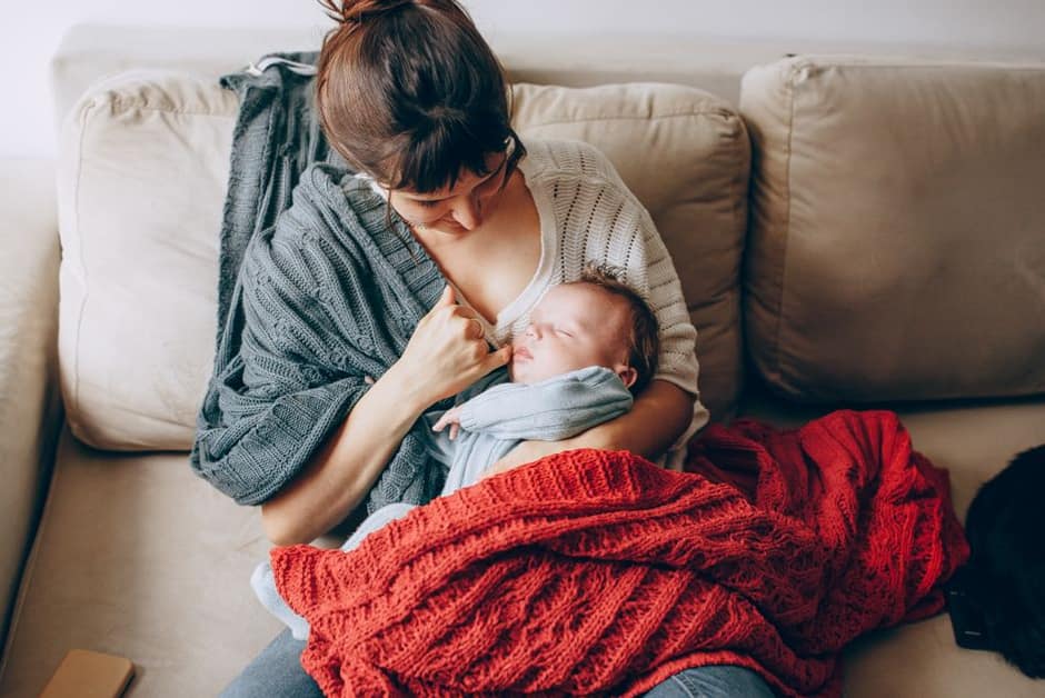 Parent tenant son bébé emmitouflé dans un plaid sur le canapé