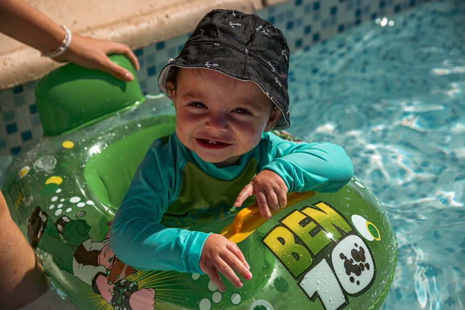 Jeune enfant souriant dans une bouée gonflable au bord d'une piscine, illustrant la vie normale avec un molluscum contagiosum