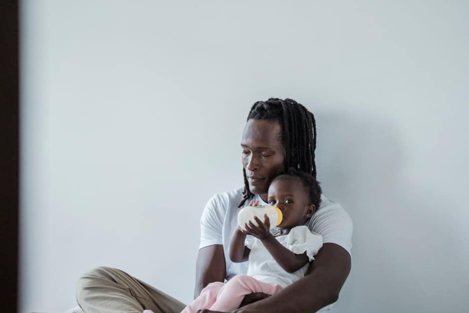 Papa donnant le biberon à son bébé calé contre lui, moment où le muguet se repère