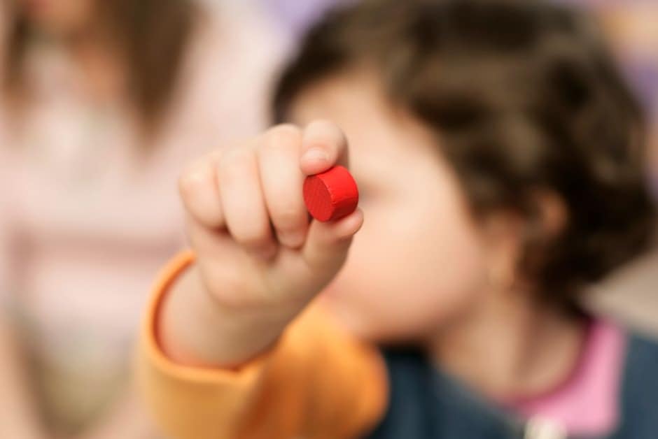 Jeune enfant jouant avec un cube en crèche, professionnelle en arrière-plan
