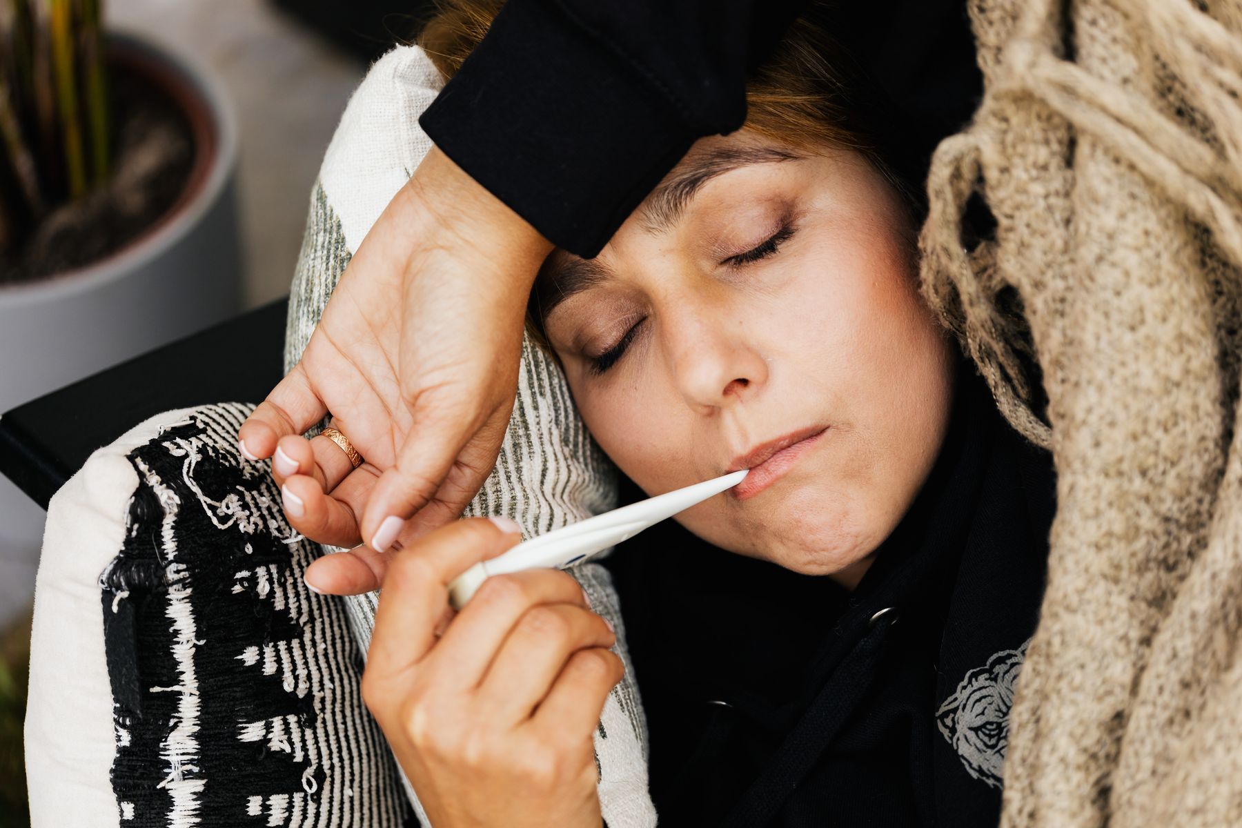 Adulte fiévreux allongé, thermomètre à la bouche, après avoir attrapé le pied-main-bouche de son enfant