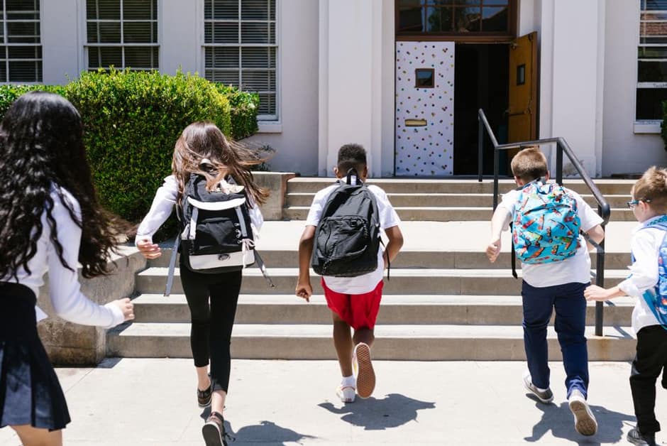 Enfants entrant dans l'école en courant, cartables sur le dos