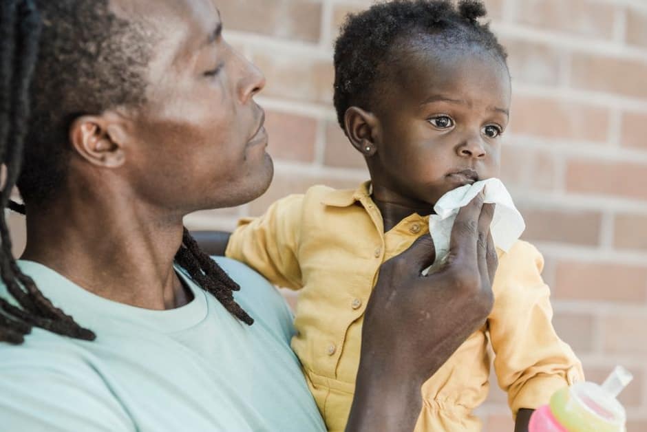 Papa essuyant doucement le nez de son bébé qu'il tient dans les bras