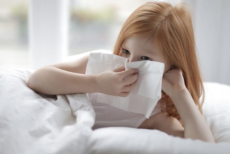 Petite fille enrhumée au repos dans son lit, mouchoir à la main