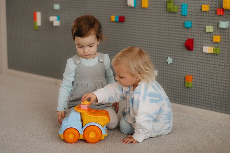 Deux jeunes enfants assis par terre jouent ensemble avec des jouets colorés à la crèche