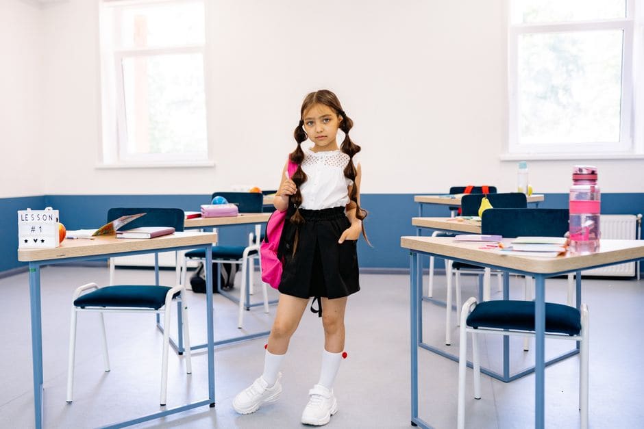 Une écolière avec un cartable rose se tient debout seule dans une salle de classe