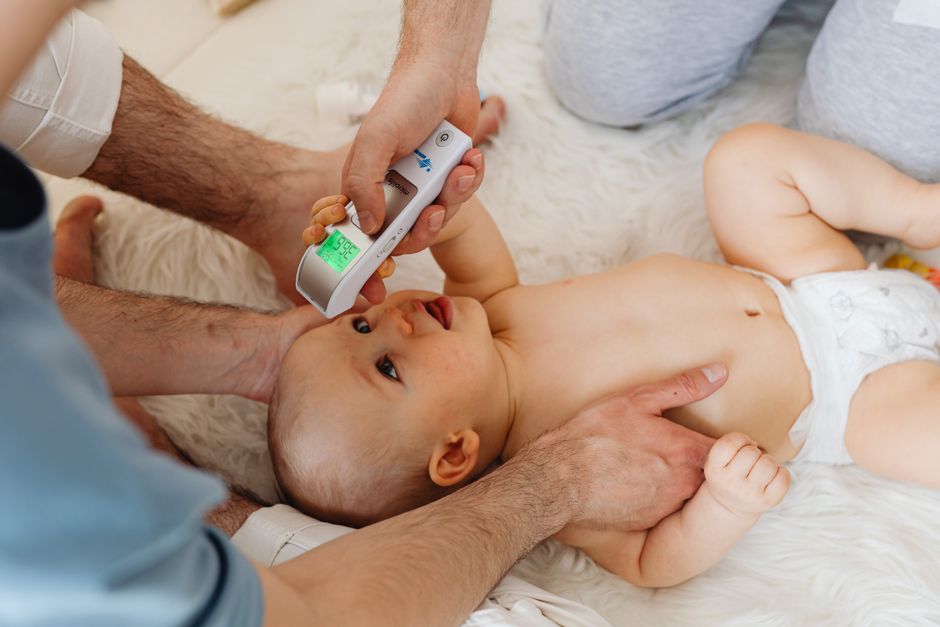 Parent prenant la température d'un bébé au front avec un thermomètre sans contact, à la maison
