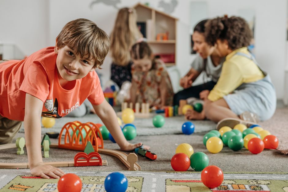 Enfants jouant ensemble dans une salle de jeux de crèche, encadrés par des professionnelles de la petite enfance