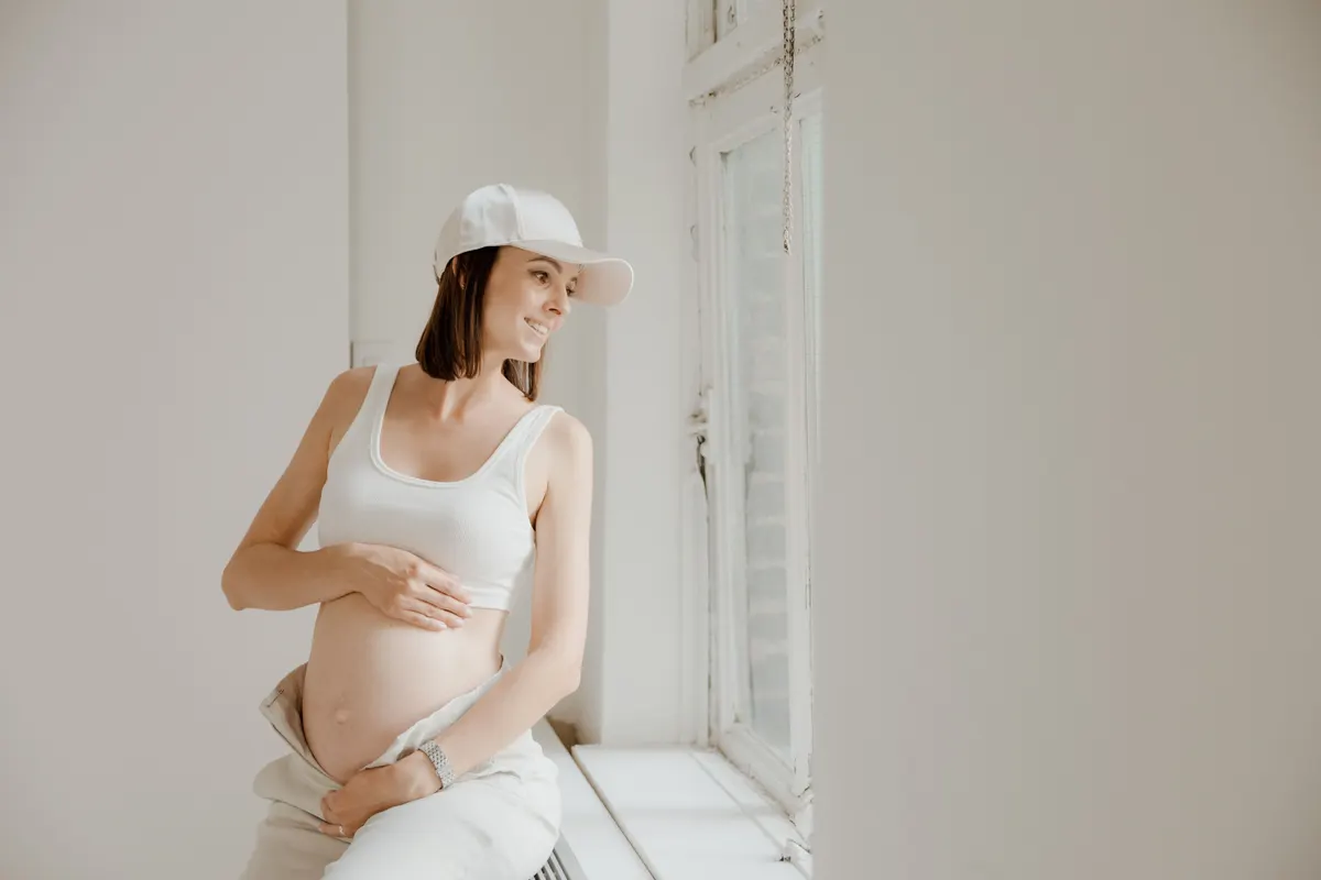 Femme enceinte assise près d'une fenêtre, une main sur le ventre