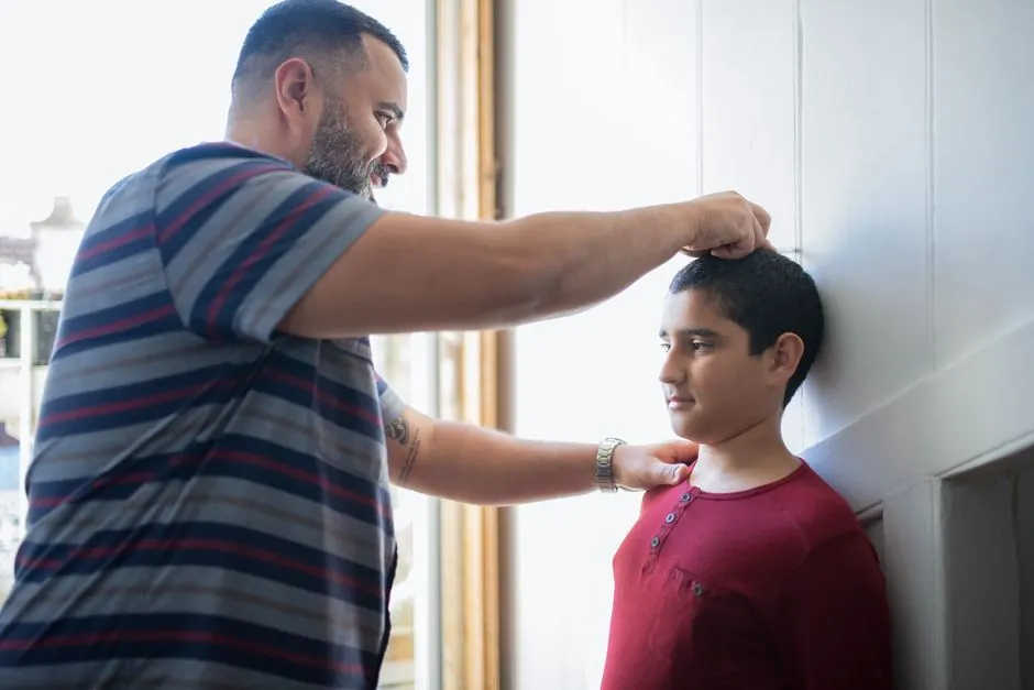 Un père mesure son adolescent contre le mur de la maison