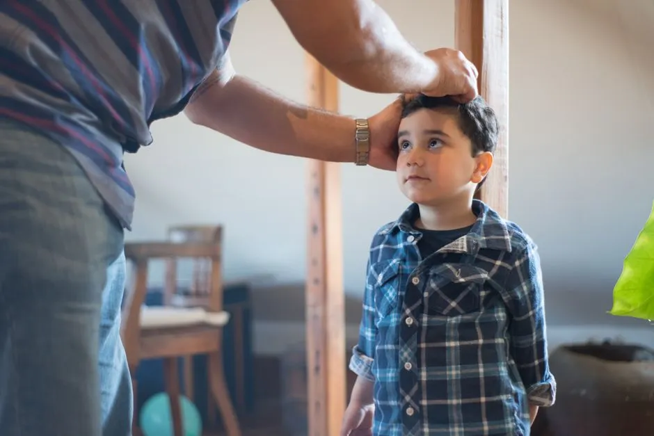 Un père mesure la taille de son jeune fils sur une toise en bois à la maison