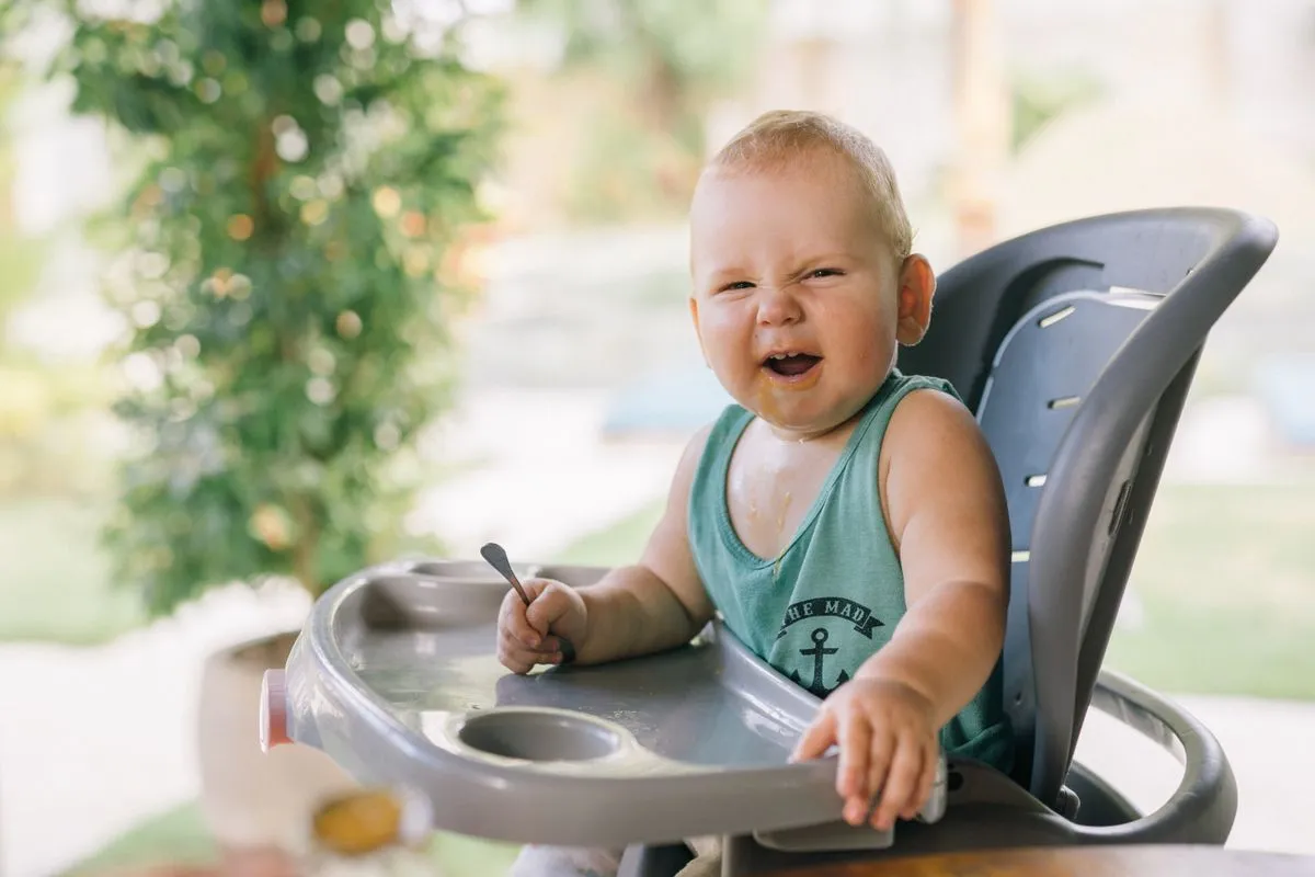 Bébé de 7 mois dans sa chaise haute, cuillère à la main